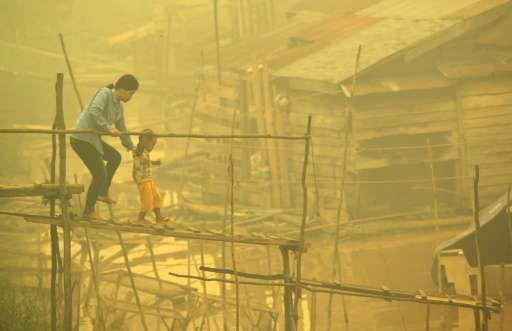 An Indonesian woman and a child walk on a bamboo bridge as thick yellow haze shrouds the city in Palangkaraya on October 22, 201