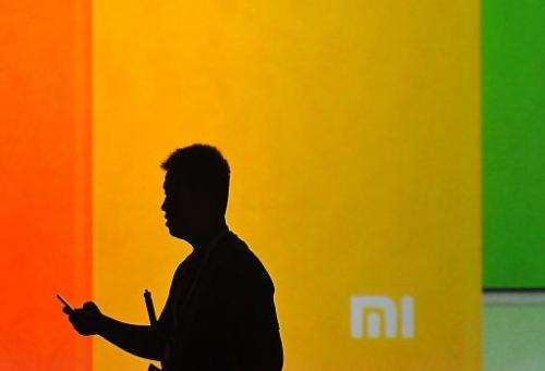 A man looks at his mobile phone as he walks past a screen displaying the Xiaomi logo. AFP Photo / Wang Zhao