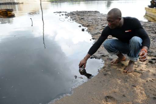 A man scoops spilled crude oil into a bottle from the waters of the Niger Delta swamps of Bodo, a village in Ogoniland, on June 