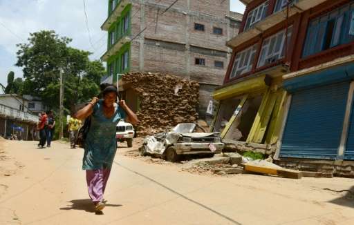 A Nepalese woman carries a load as she walks past destroyed buildings in Chautara on June 30, 2015, following twin earthquakes w