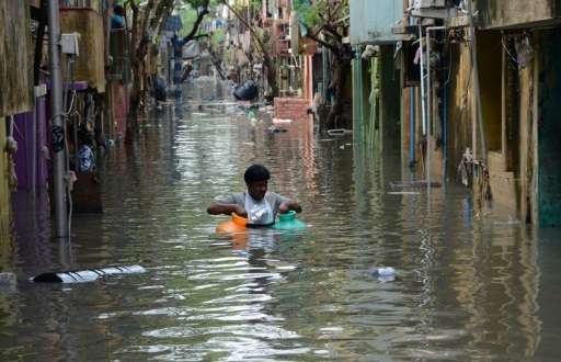 An Indian man carries gas canisters through floodwaters on a street in Chennai on December 4, 2015