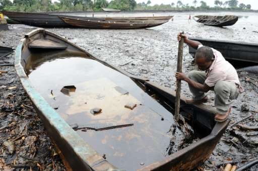 An indigene of Bodo, in Nigeria's Ogoniland region, tries to separate with a stick the crude oil from water in a boat at the Bod