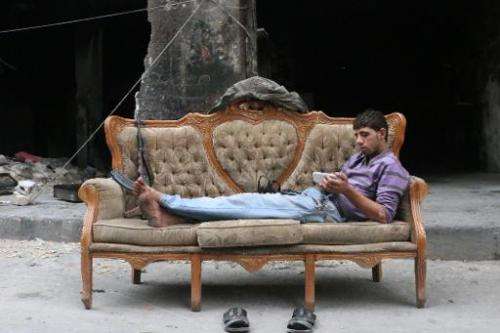 A rebel fighter looks at his smartphone lying on a sofa on October 23, 2014, in Bustan Pasha neighbourhood of Syria's northern c