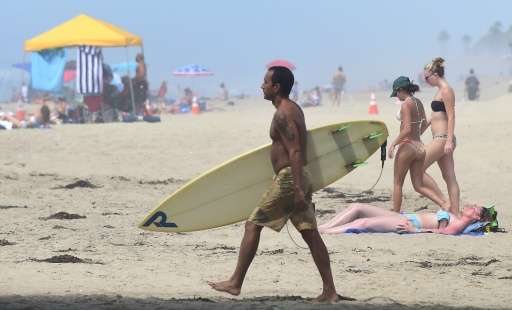 A surfer carries his board past sunbathers at Huntington Beach on September 10, 2015, amid a heat wave where temperatures have r