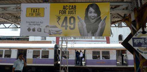 A train waits below an advertisement for an app-based taxi-hailing service, at a railway station in Mumbai