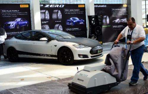 A worker pushes his machine past a 2014 Tesla P85s on display at the LA Auto Show in November 2014