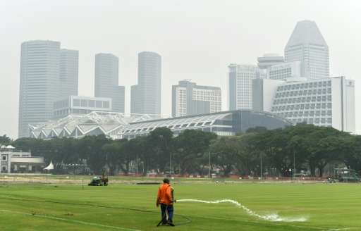 A worker waters a field as downtown buildings are shrouded in smog in Singapore on October 5, 2015