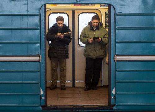 Commuters consult their electronic connected devices inside a train coach in the Moscow Metro on December 1, 2014