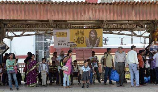 Commuters wait for a train below an advertisement for a app-based taxi-hailing service, on a railway platform in Mumbai