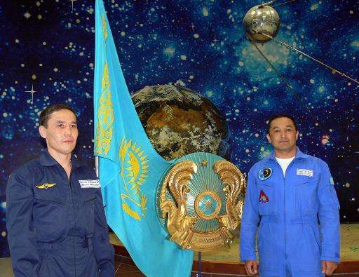 Kazakh cosmonaut candidates Mukhtar Aimakhanov (L) and Aidyn Aimbetov pictured next to their national flag and a model of the fi