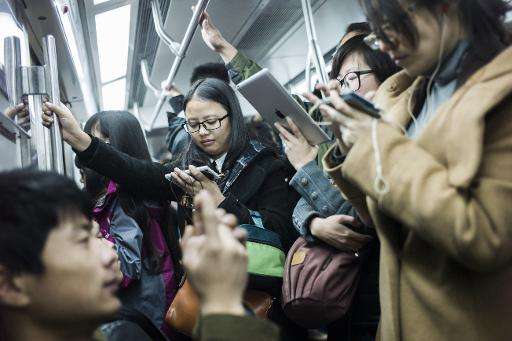 People use their smartphones during the morning rush-hour in Beijing, in November 2014