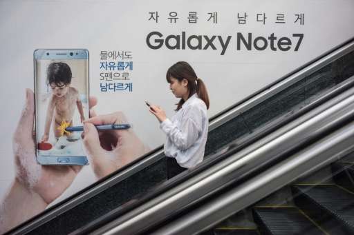 A woman looks at her mobile phone as she rides an escalator past an advertisement for Samsung's Galaxy Note 7 device in Seoul on