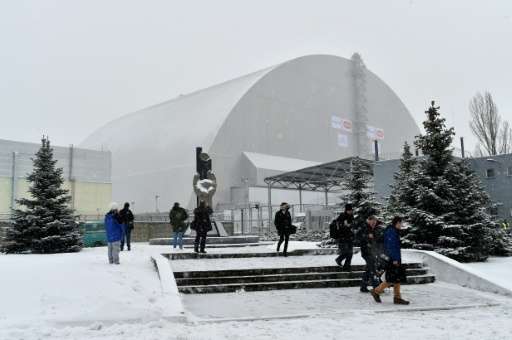 People walk past Chernobyl's New Safe Confinement covering the destroyed 4th block of the Chernobyl nuclear power plant after it