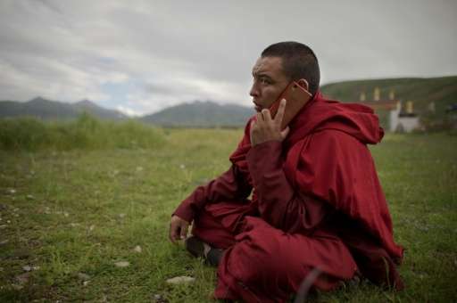 A Buddhist monk talks on his smartphone as he sits on the grassland of the Tibetan Plateau in Yushu County