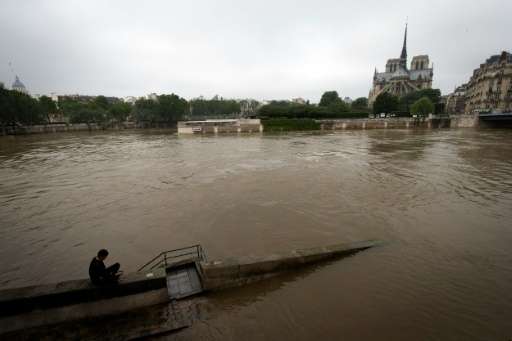 A man sits on a low wall by the rain-swollen river Seine and Notre Dame De Paris cathedral on June 5, 2016 in Paris