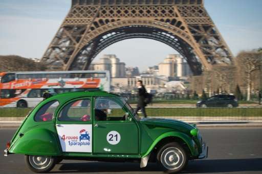 An employee of the French tourist company Four Wheels Under an Umbrella drives a Citroen 2CV electric car close to the Eiffel to