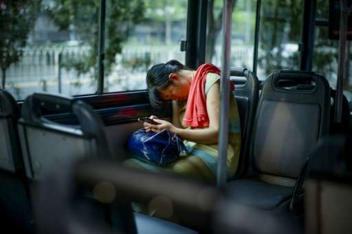 A passenger holds her mobile phone while asleep on a bus in Beijing