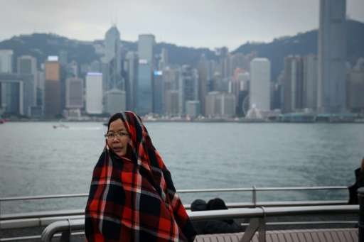 A woman on a viewing deck next to Victoria Harbour in the Tsim Sha Tsui district of Hong Kong keeps warm by wrapping herself a b