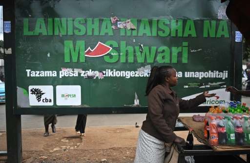 A woman sells beverages at a bus stop near an advertisement for a mobile hone-based banking service, in the Kenyan capital Nairo