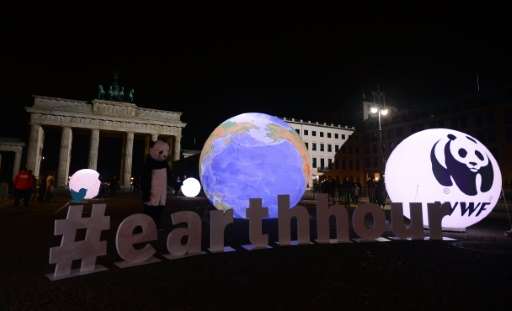 A WWF activist dressed as a panda bear stands next to an illuminated globe in front of the darkened Brandenburger Gate in Berlin