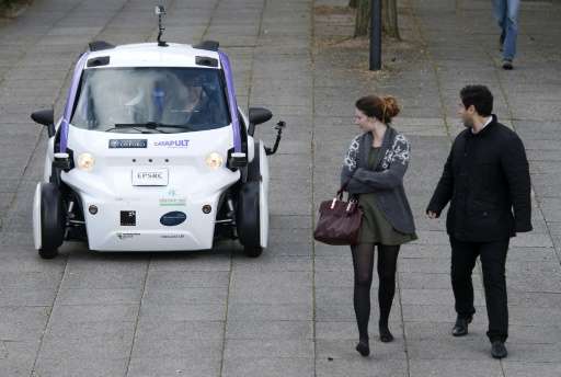 Bystanders look at an autonomous self-driving vehicle as it is tested in a pedestrianised zone during a media event in Milton Ke