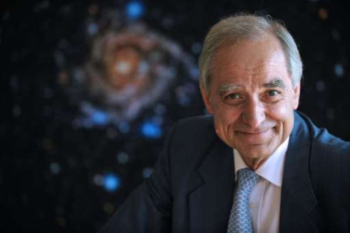 French astrophysician Andre Brahic poses in front of a picture of the IC 342 galaxy at the headquarters of the French Atomic ene
