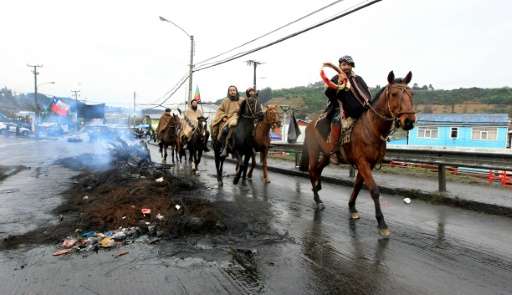 Local residents riding horses pass along a burnt out barricade in a street of Castro, Chiloe island on May 9, 2016