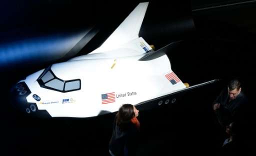 People stand next to a model of a new space shuttle designed by US company Sierra Nevada Corporation (SNC)