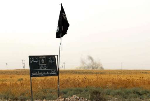 Smoke rises in the distance behind an Islamic State group (IS) flag and banner on September 11, 2015