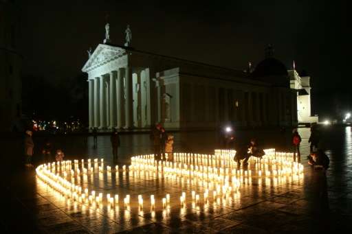 People attend a candle light vigil at the Vilnius Cathedral as it stands unlit during Earth Hour
