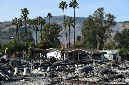 Firefighters comb through smoldering ash in the remains of dozens of homes destroyed by the Lilac Fire in Fallbrook, California