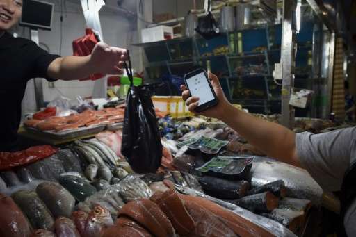 This photo taken on June 27, 2017 shows a man making purchases through his smartphone at a seafood booth at a market in Beijing