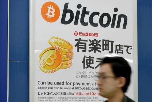 A man walking past a signboard in Tokyo informing customers that Bitcoin can be used for payment, as more and more major compani