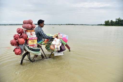 An Indian vendor pushes a bicycle carrying his wares through floodwaters in Balimukh Ashigarh village in Morigoan district, in I