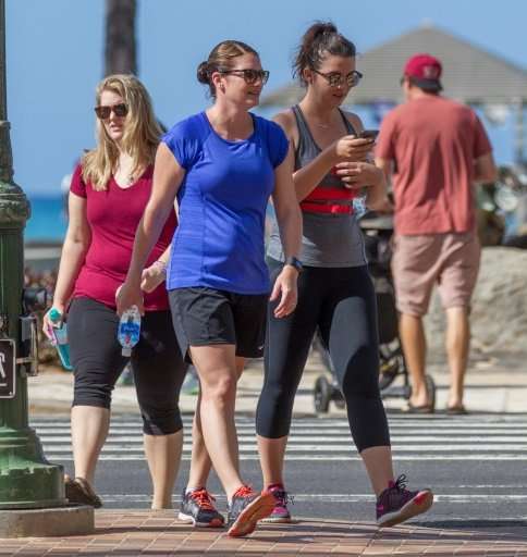 A visitor crosses an avenue in Honolulu looking at her cell phone, behavior the city regards as a menace to public safety