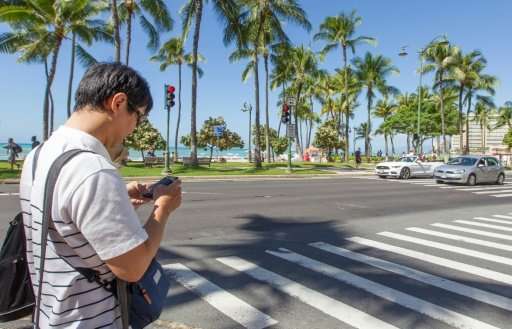 A visitor texts before crossing the street in the Honolulu beachside neighborhood of Waikiki on October 24, 2017, on the eve of 
