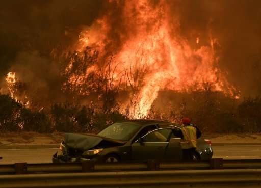 A woman involved in a traffic accident waits to get towed beside a wall of flames on the 101 highway during the Thomas wildfire 