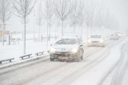 Cars drive slowly along a snow-covered road in Rotterdam during heavy snowfall.