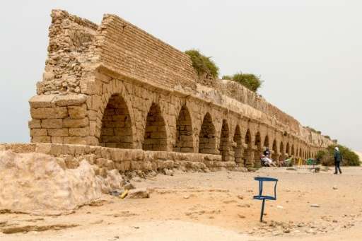 People sit next to an ancient aqueduct in the Roman-era city of Caesarea which is set for renovation as part of a multi-million-