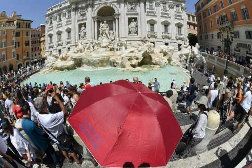 Sightseers shelter from the sun under an umbrella in front of Trevi fountain in Rome as temperatures reached more than 40 degree