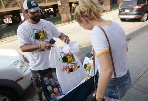 T-shirt vendor Jan Dahouas shows an eclipse t-shirt of his own design to a buyer on a street near the City Market in Charleston,
