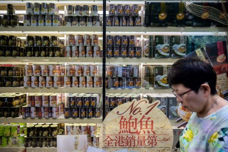 A woman walks past a shop with a window display of tinned abalone products in Hong Kong