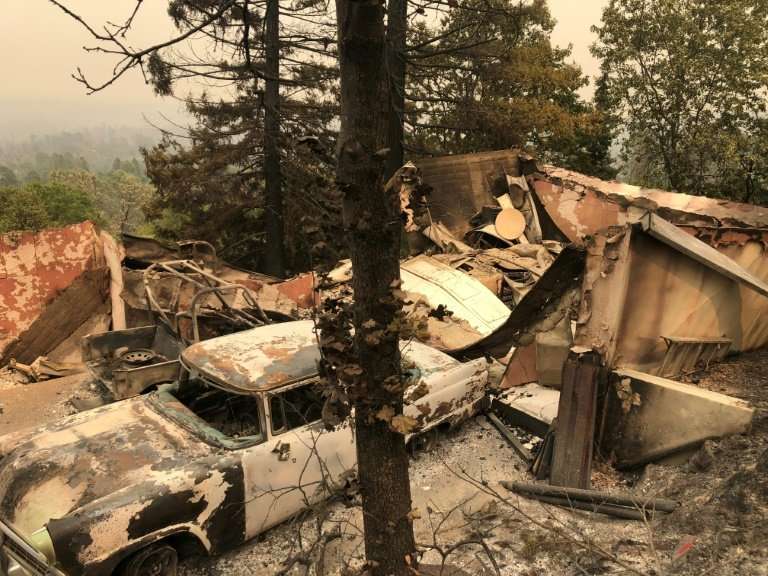 The remains of an antique car collection lie in a fire devastated neighborhood near Redding, California, as firefighters from ac