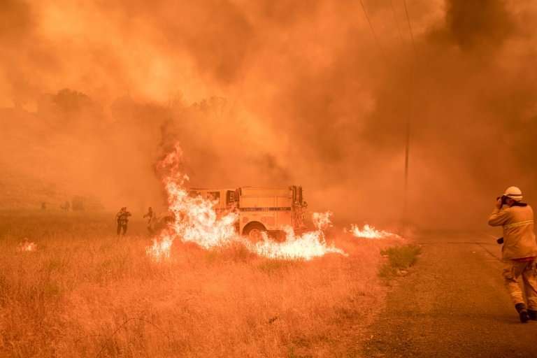 Firefighters scramble to control flames surrounding a fire truck as the Pawnee fire jumps across highway 20 near Clearlake Oaks,