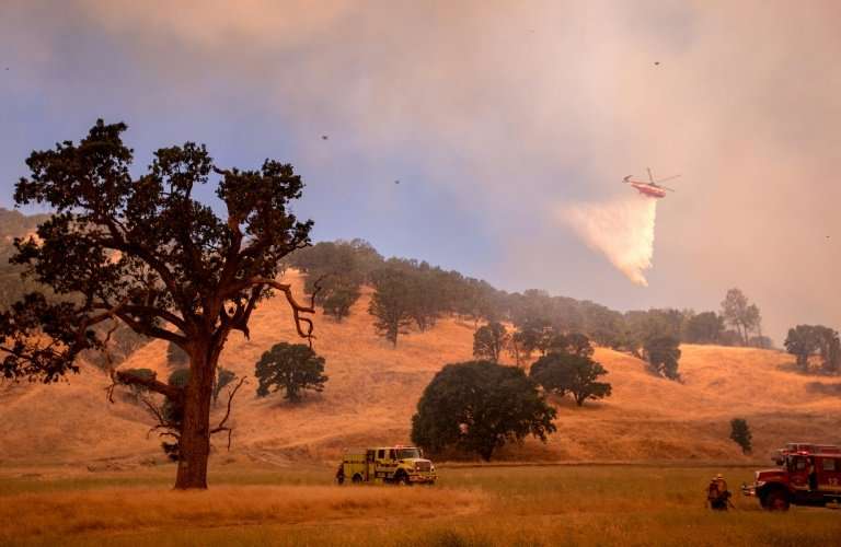 A helicopter drops water on a hillside as firefighters scramble to get control as flames from the Pawnee fire near Clearlake Oak