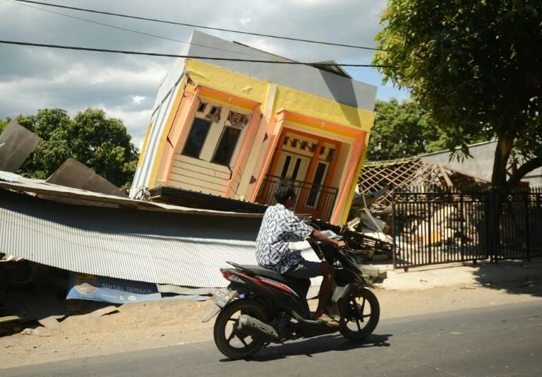 A man riding a motorcycle passes by a damaged house at Sira village in northern Lombok