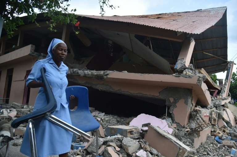 A nun carries chairs near a school damaged by a weekend earthquake in Haiti that has now left at least 17 people dead