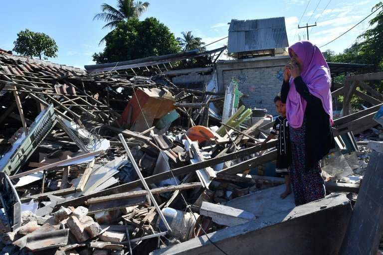 A woman and boy watch as men clear the wreckage of houses damaged by an earthquake in Menggala, North Lombok