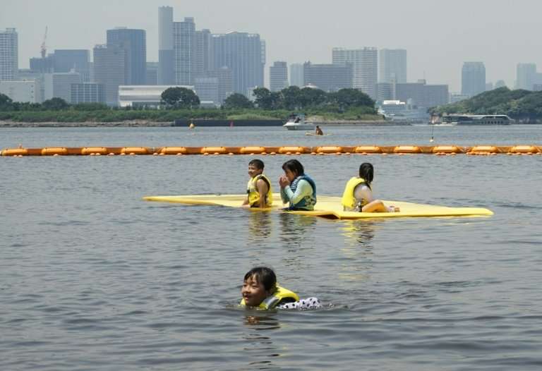 Children swim at Odaiba seaside park in Tokyo Bay with the skyline of the world's biggest city shimmering behind them