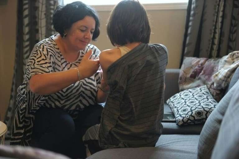 Melanie Ferrer helps her son Julien with one of the three injections he needs per week to treat his condition